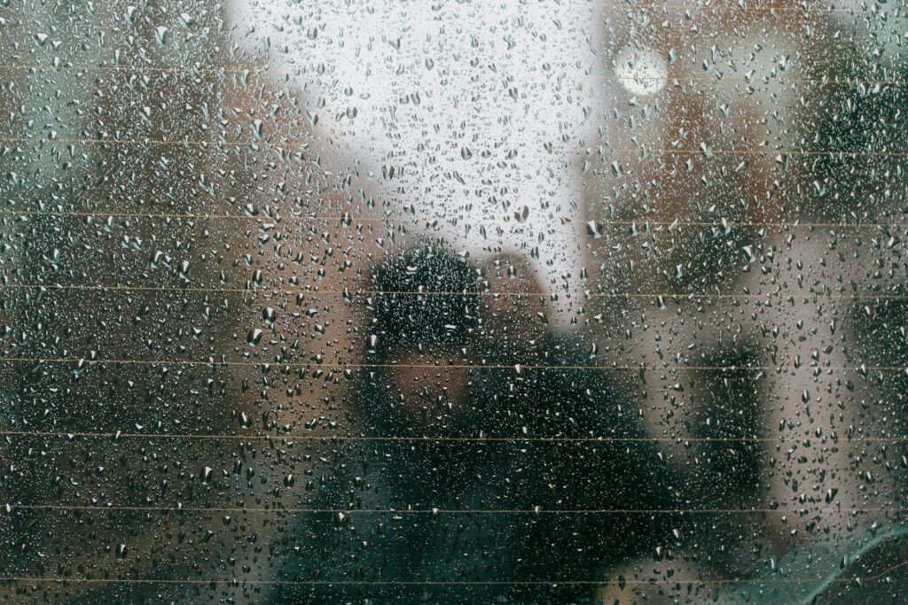 Raindrops on a car window with blurry figures outside.