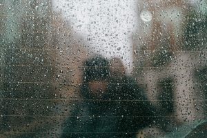 Raindrops on a car window with blurry figures outside.