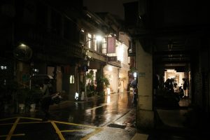 Rainy night in a narrow city alleyway with glowing lights.